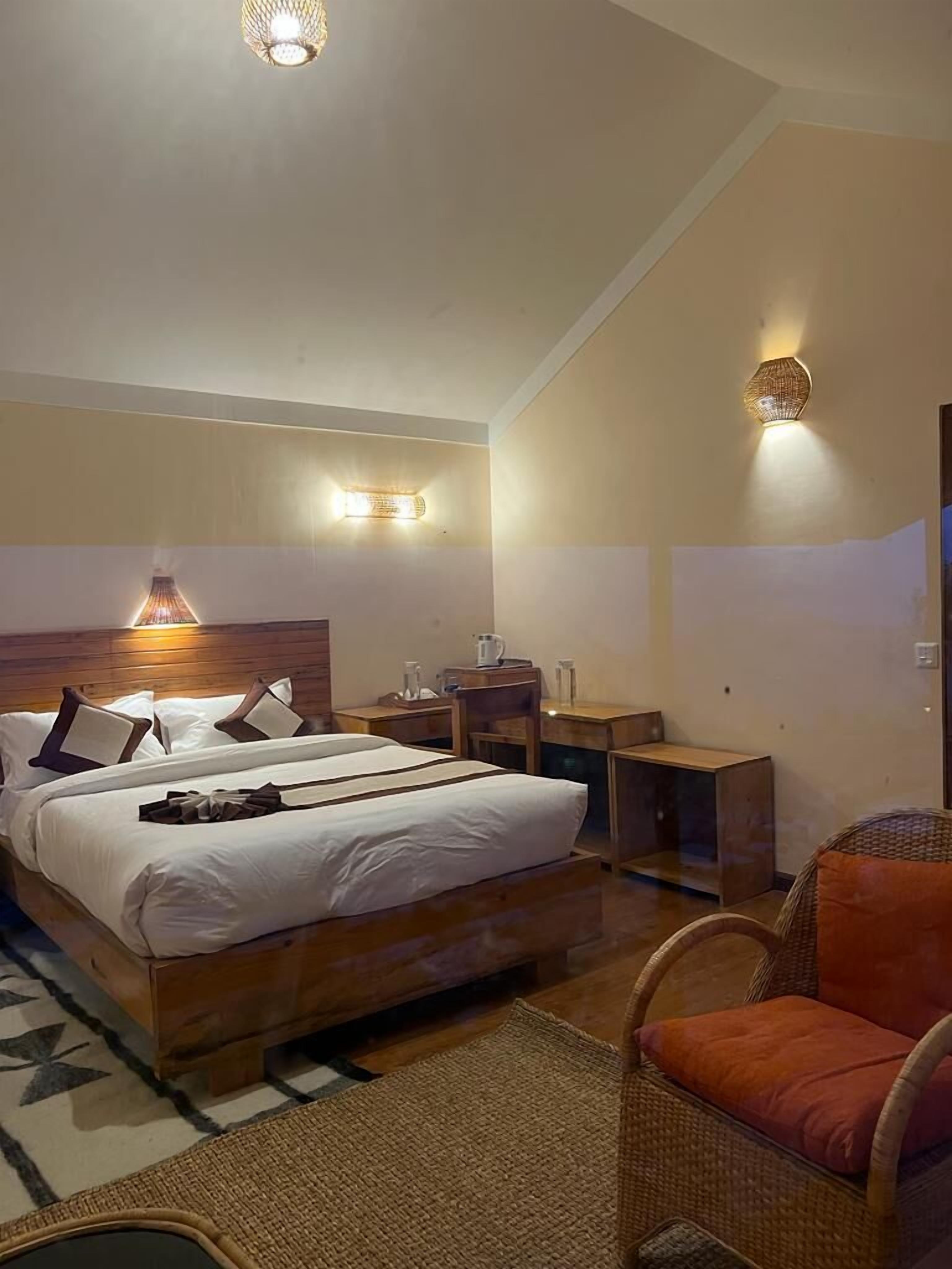 A bedroom with a large bed, two bedside tables, a chair, a desk, and two wall-mounted lights.