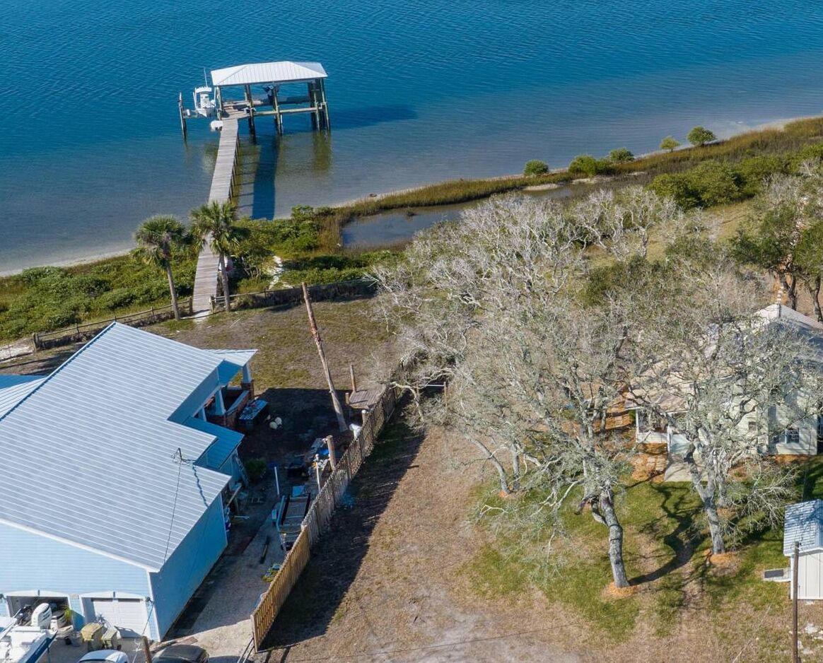 Eine Luftaufnahme eines Anwesens an der Küste mit einem Steg, der ins Wasser führt, einem Haus mit blauem Dach und freiem Blick auf die umliegende Landschaft.