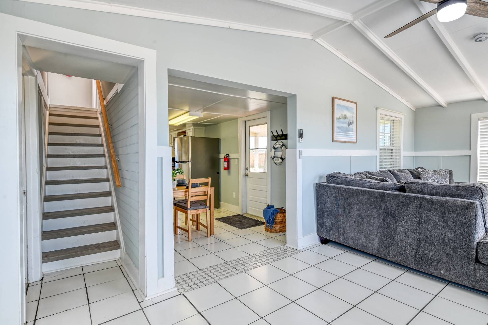 A spacious living area with a grey sofa, a staircase, and a kitchen visible through an open door.