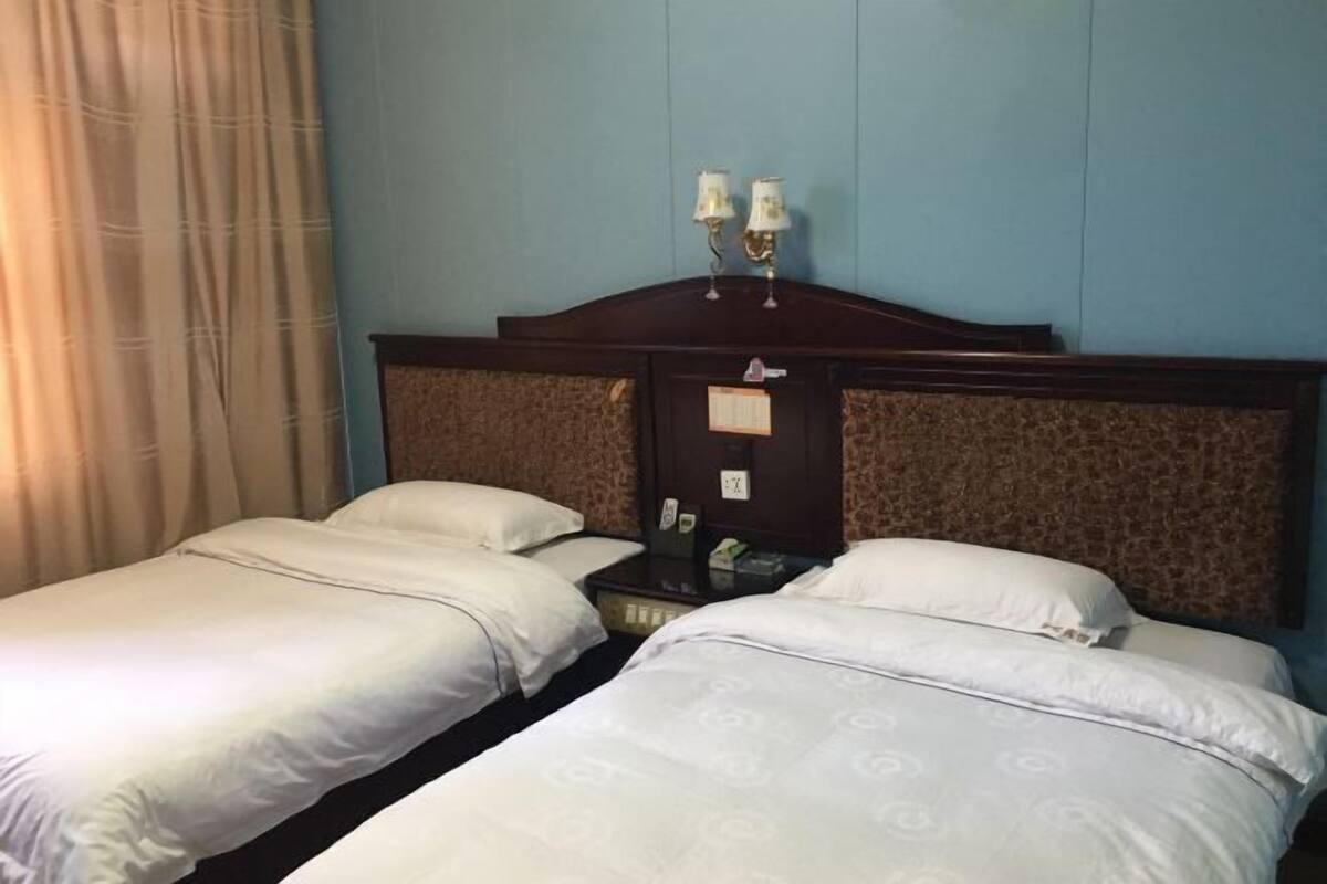 Habitación de hotel con dos camas, una mesita de noche, una lámpara y una ventana con cortinas.