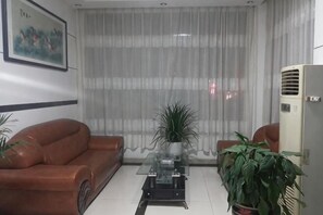 A living room with a brown leather sofa, a glass coffee table, a potted plant, a large window with sheer curtains, and a white air conditioning unit. - Shuangfeng Century Hotel (Shuangfeng)