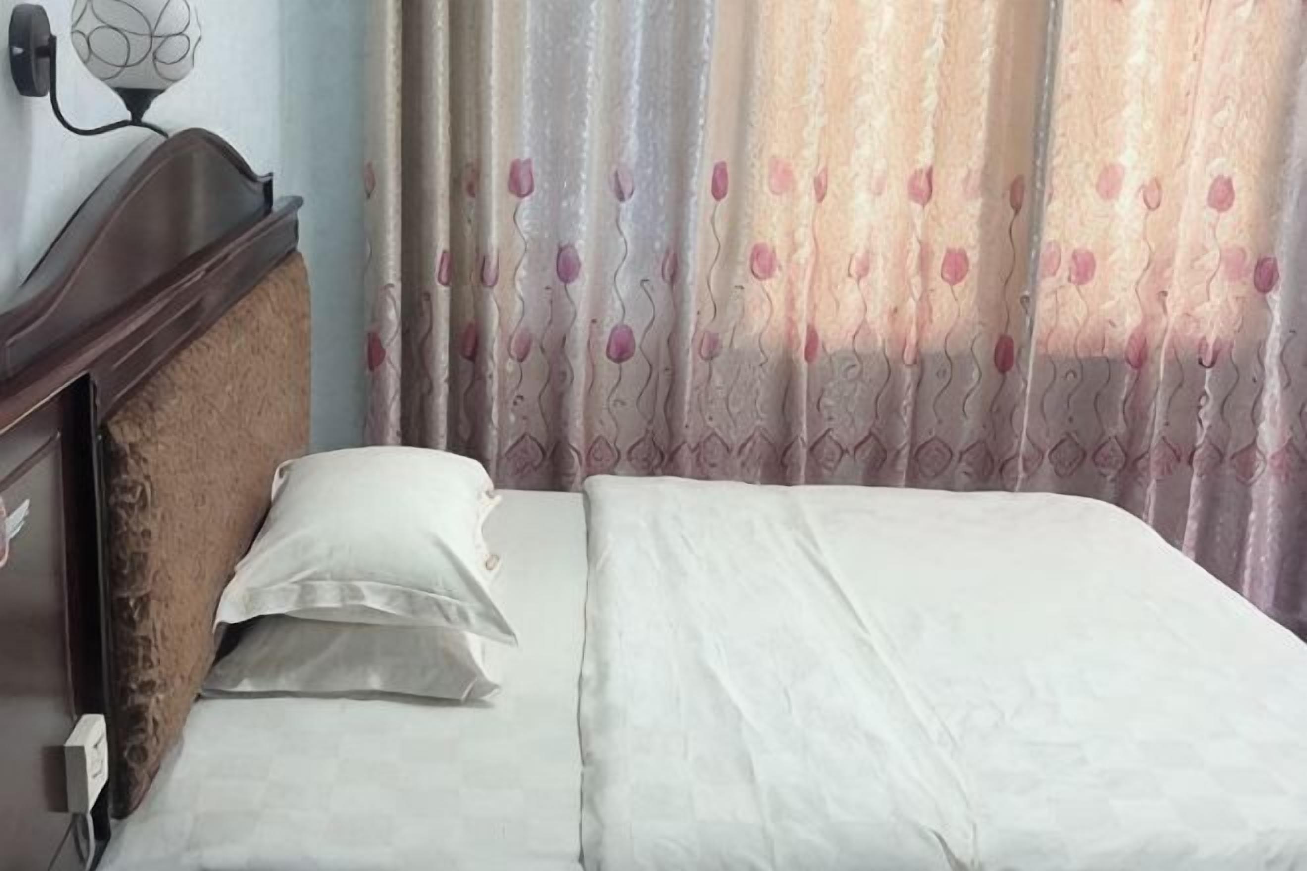 Una cama con sábanas blancas, cabecera de madera y lámpara de pared.