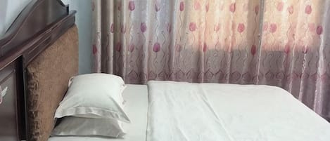 A bed with white linens, a wooden headboard, and a wall-mounted lamp.