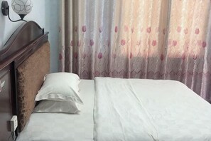 Un lit avec du linge de lit blanc, une tête de lit en bois et une lampe fixée au mur.