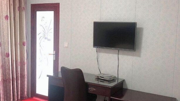 A room with a TV mounted on the wall, a desk with a chair, and a door with a frosted glass panel. - Shuangfeng Century Hotel (Shuangfeng)