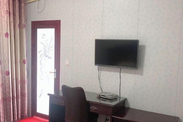 Une pièce avec un téléviseur fixé au mur, un bureau avec une chaise et une porte dotée d’un panneau en verre dépoli.