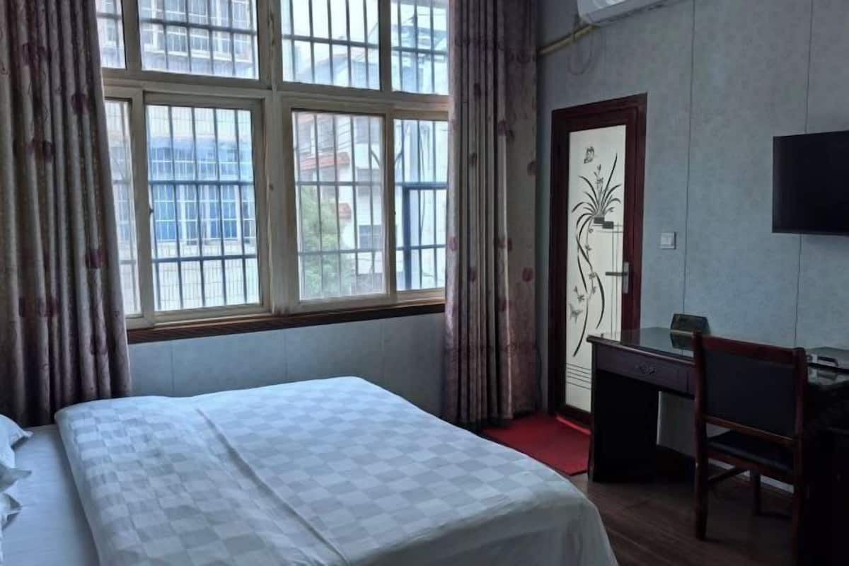 Habitación de hotel con cama, escritorio, silla, televisor y ventana con cortinas.