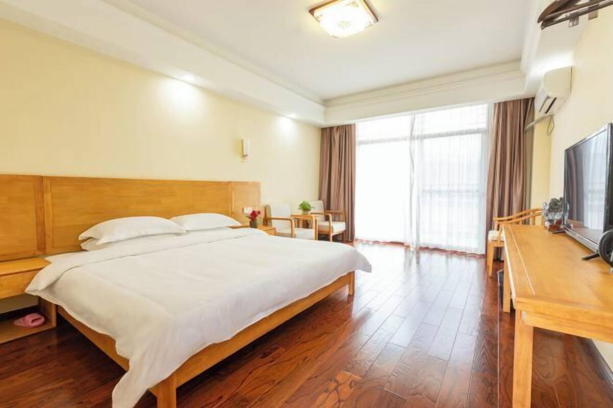 Habitación de hotel con una cama grande, suelo de madera, un escritorio con silla, televisor y ventana con cortinas.