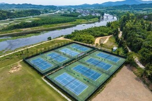 Ovenfra ses et tennisanlæg med flere baner, omgivet af grønt og en flod.