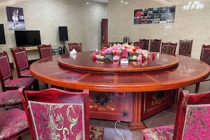 Una sala de conferencias con una mesa redonda, sillas tapizadas en rojo y un centro de mesa floral.