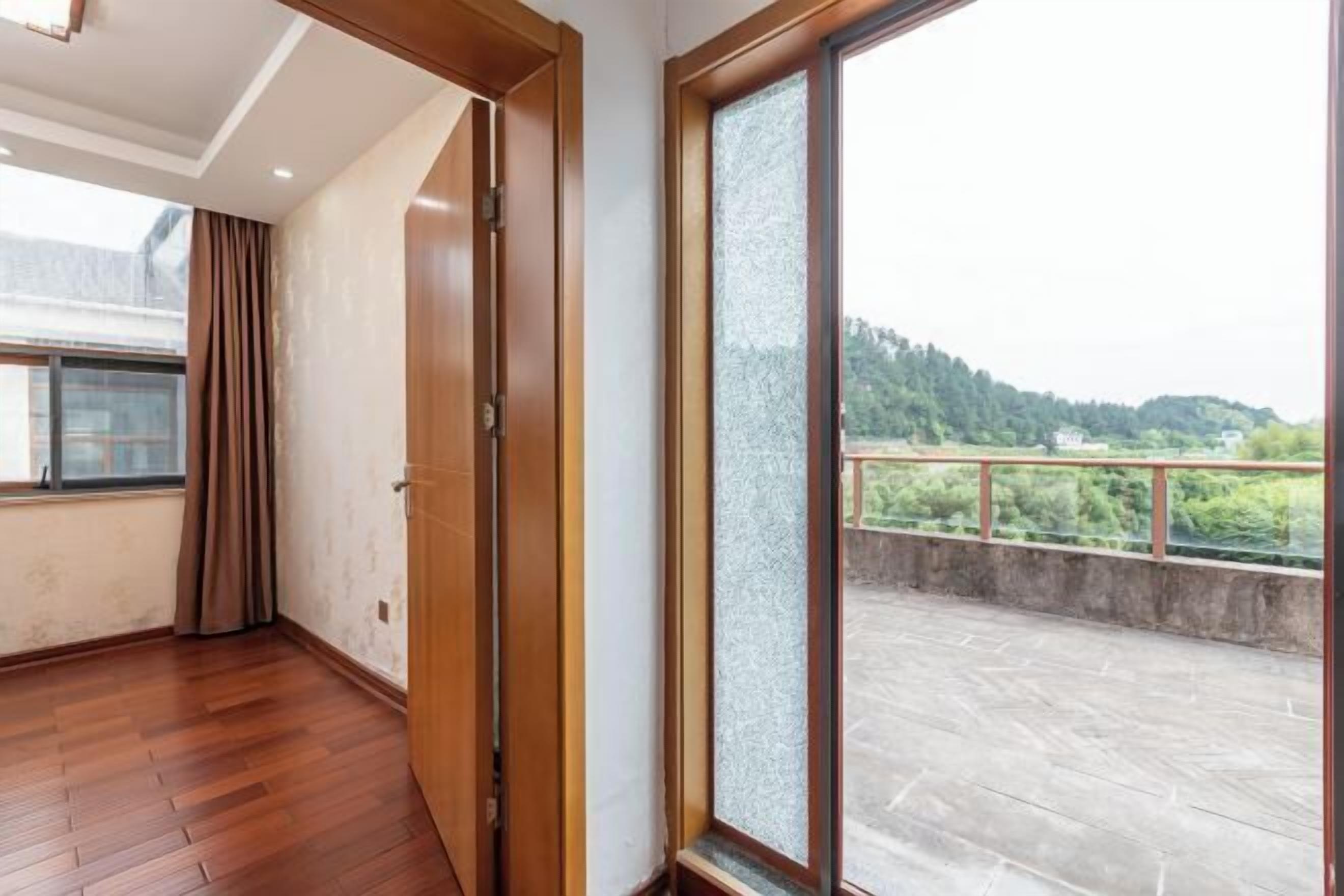 A room with wooden flooring, a sliding glass door, and a view of a balcony with a railing.