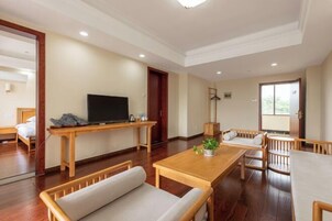 Uma sala de estar moderna com televisão, mobiliário de madeira, uma mesa de jantar e vista através de uma porta de vidro.