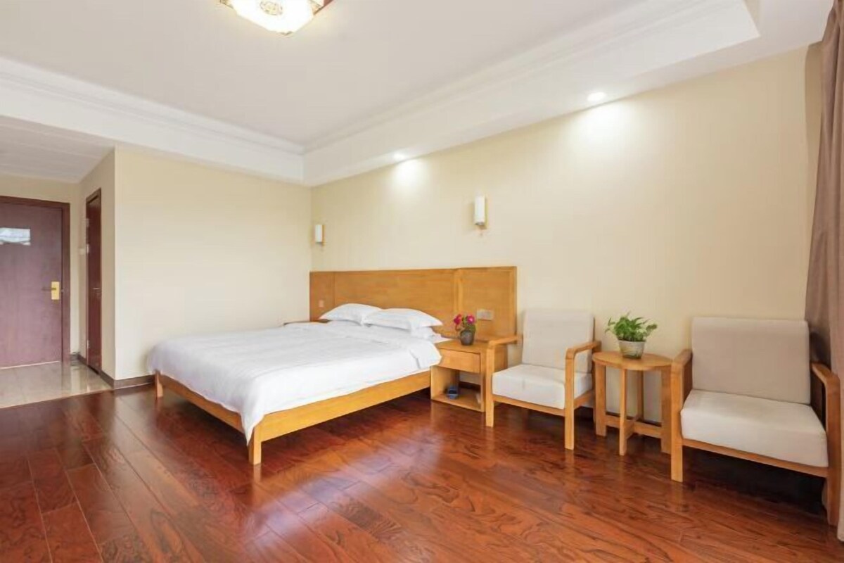 Une chambre d’hôtel avec un lit en bois, deux chaises, une petite table avec une plante et une table de chevet.
