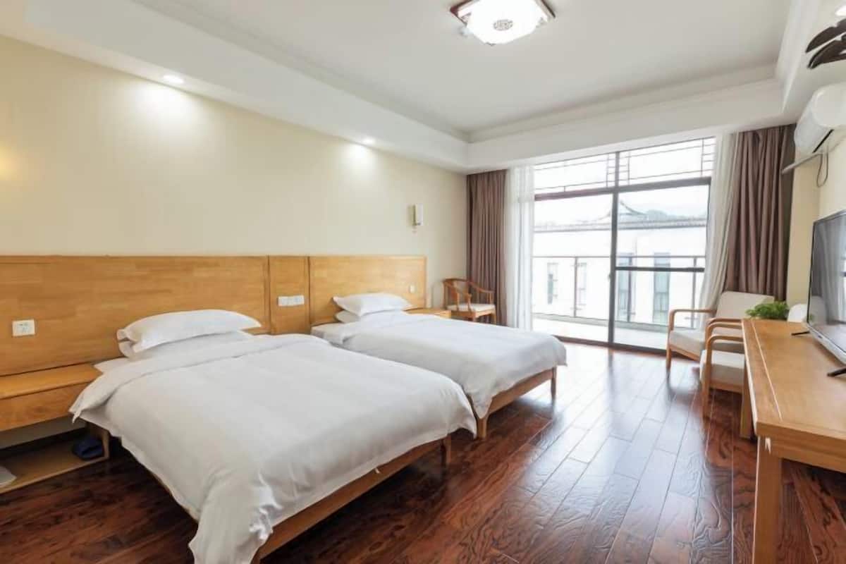Habitación de hotel con dos camas, un escritorio de madera, una silla y un ventanal con vistas.
