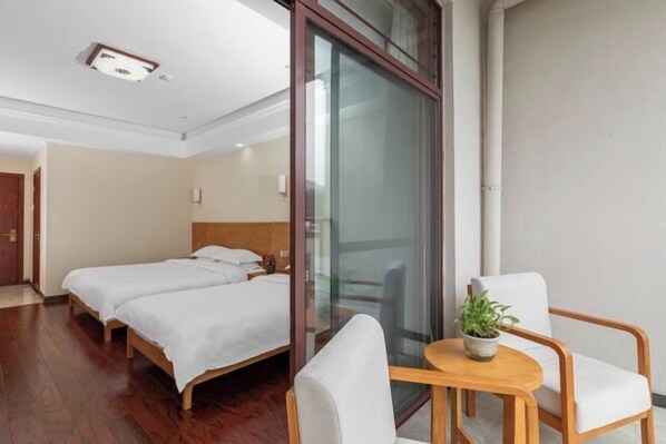 Une chambre d’hôtel avec deux lits, une cloison en verre, une petite table avec une plante et une chaise.