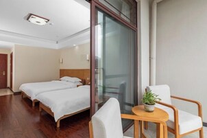 Habitación de hotel con dos camas, un separador de vidrio, una mesita con una planta y una silla.