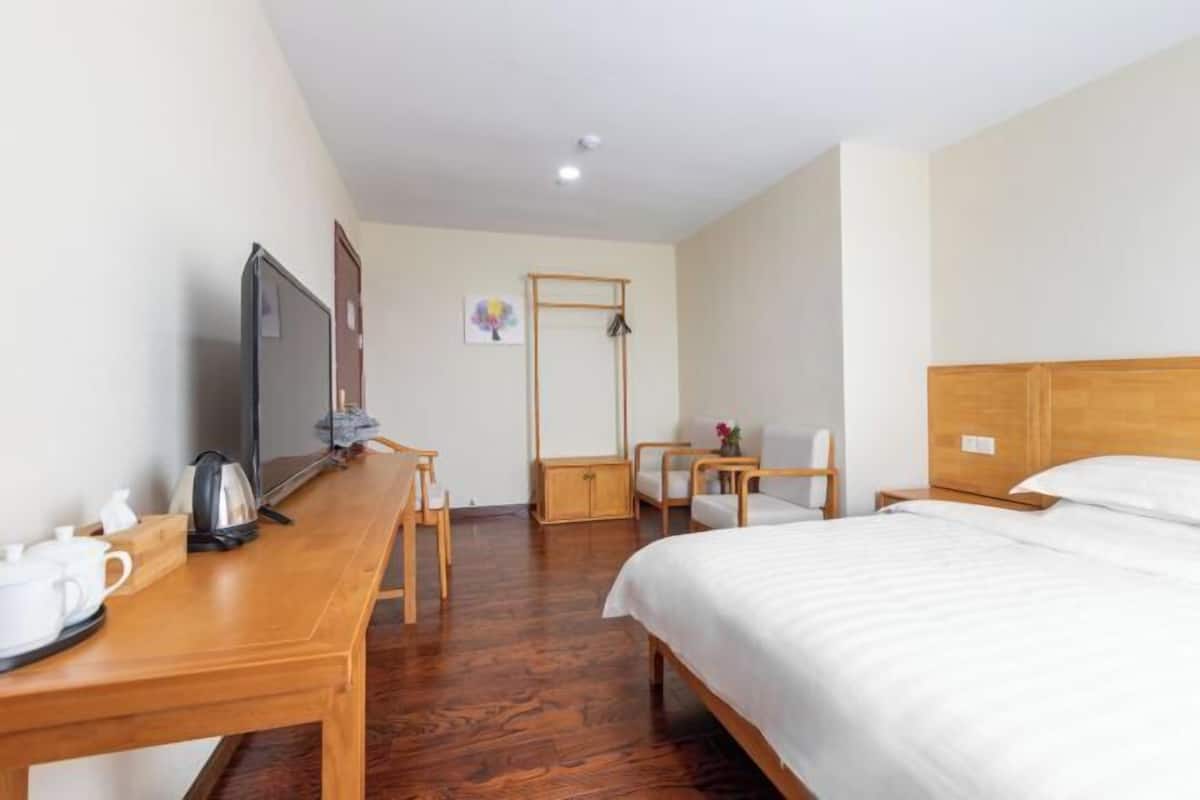 Habitación de hotel con cama de madera, escritorio con televisor, una silla y una mesita con tetera y tazas.