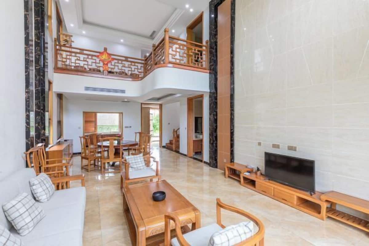 Amplia sala de estar con techo alto, muebles de madera, televisor y un balcón con detalles arquitectónicos chinos tradicionales.