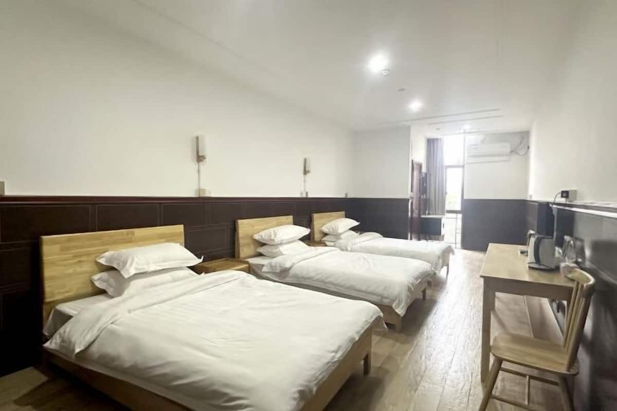 Habitación de hotel con tres camas individuales, cabecero de madera, escritorio con silla y televisor.