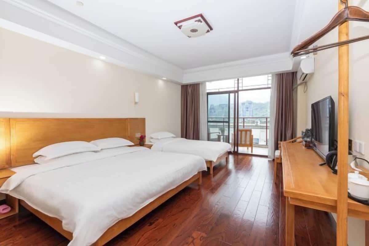 Habitación de hotel con dos camas, un escritorio de madera, televisión y balcón con vistas.