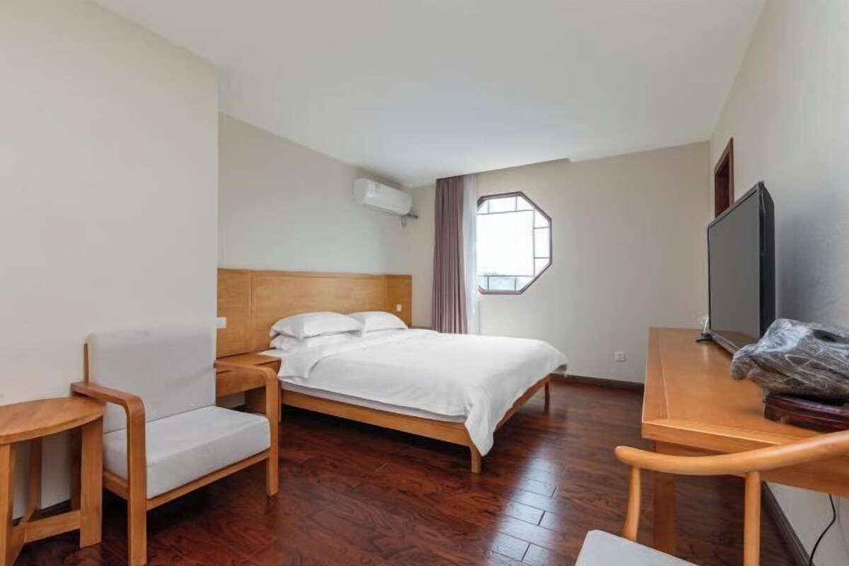Une chambre d’hôtel avec un lit, une télévision, une chaise en bois, une petite table et une fenêtre.