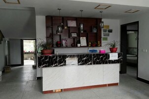 Un mostrador de recepción con encimera de mármol, rodeado de estantes con diversos objetos y plantas en macetas.