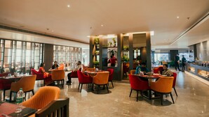 A modern restaurant with high ceilings, glass partitions, and red and orange chairs. - Raj Meridian (Dibrugarh)