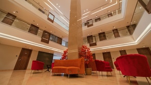 A multi-level atrium with a central pillar, red upholstered chairs, and a large potted plant. - Raj Meridian (Dibrugarh)