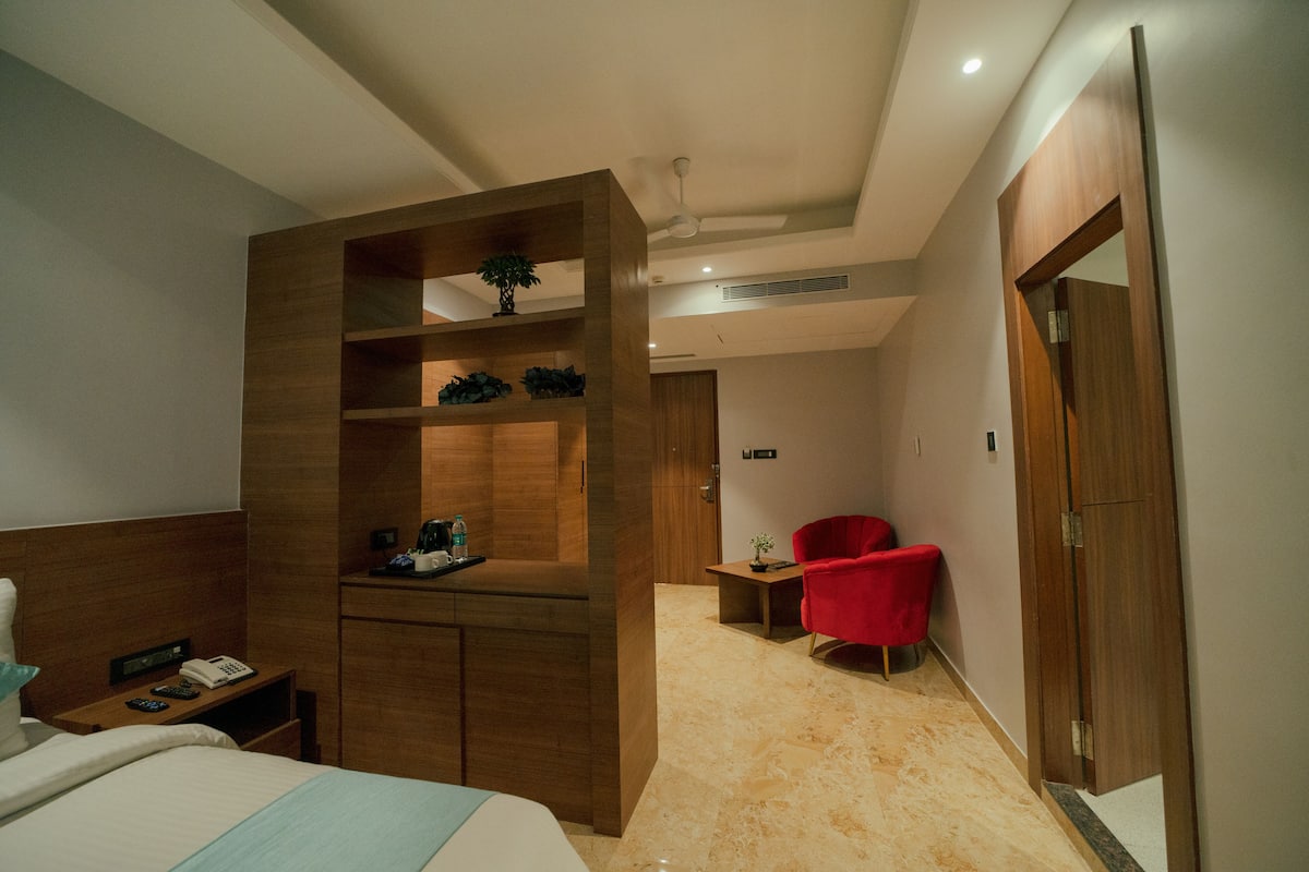 Quarto de hotel moderno com guarda-roupa de madeira, uma cadeira vermelha, uma mesinha e uma cama.