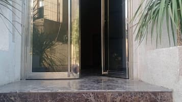 Enter a serene space through the open glass door, surrounded by lush greenery.