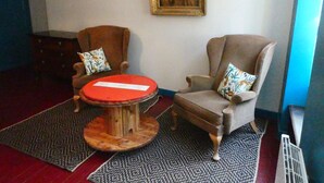 Una habitación con dos sillones, una mesa redonda de madera, alfombras estampadas y un cuadro en la pared.