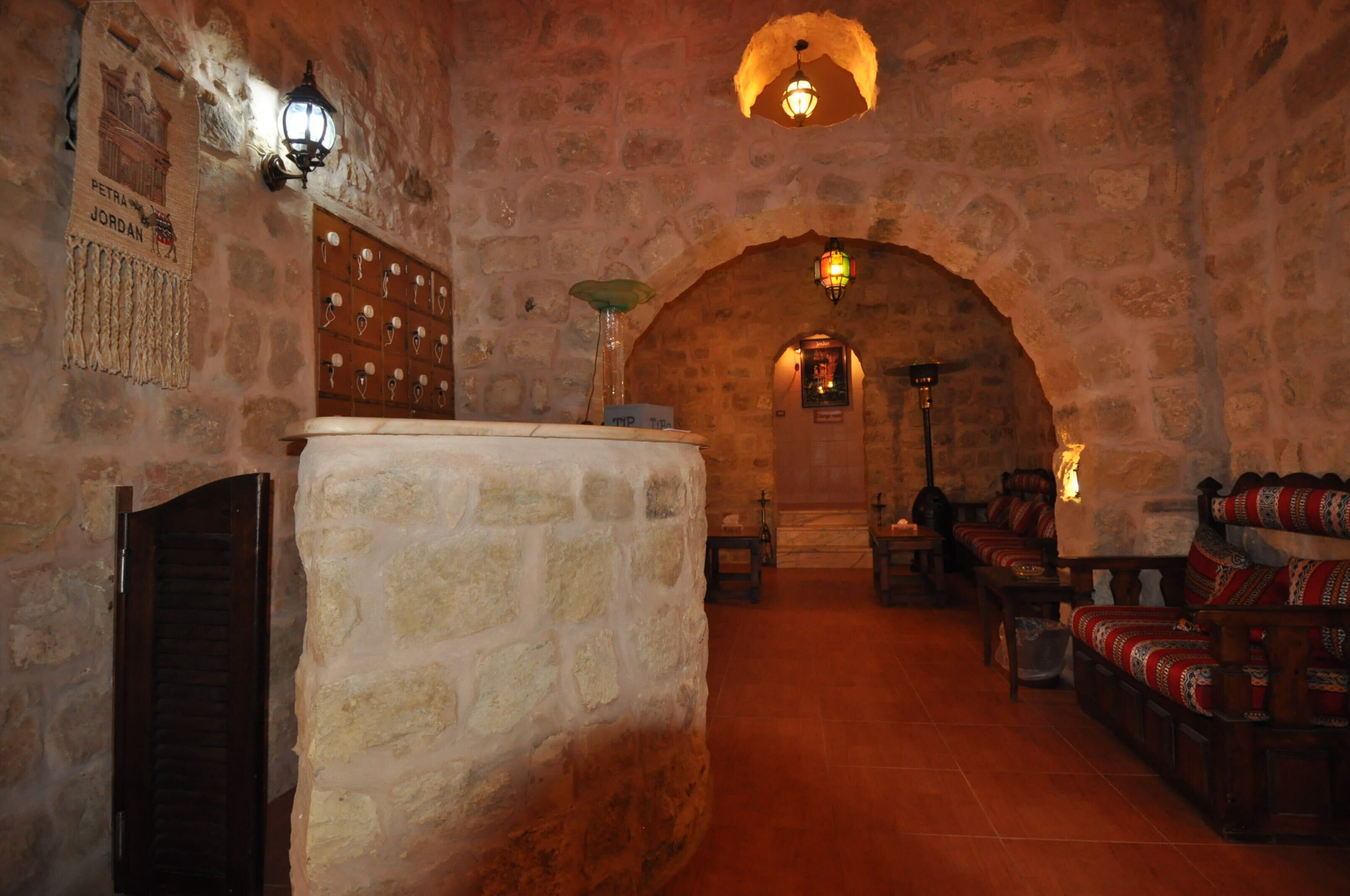 A stone-walled room with a wooden reception desk, a wooden bench, and a small table with a lamp.