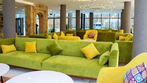 En moderne lobby med grønne sofaer og gule stole, store vinduer og en lysekrone.