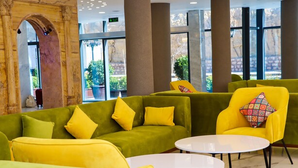 En moderne lobby med grønne sofaer og gule stole, store vinduer og en marmorgulv.