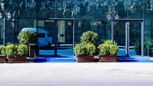 En moderne bygning med store glasfacader, der reflekterer omgivelserne. Der er plantekasser foran indgangen, og en hvid varevogn holder parkeret foran.