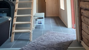 Ein Holzinnenraum mit Schlafempse, einer Holzleiter, einem Kamin und einem kleinen Tisch mit Dosen.