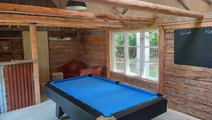 Ein Billardtisch in einem rustikalen Raum mit Holzbalken, einer Kreidetafel und einem Fenster mit Blick auf Bäume.