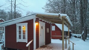 Eine kleine rote Holzhütte mit einer Holzveranda und Stufen zum Eingang.