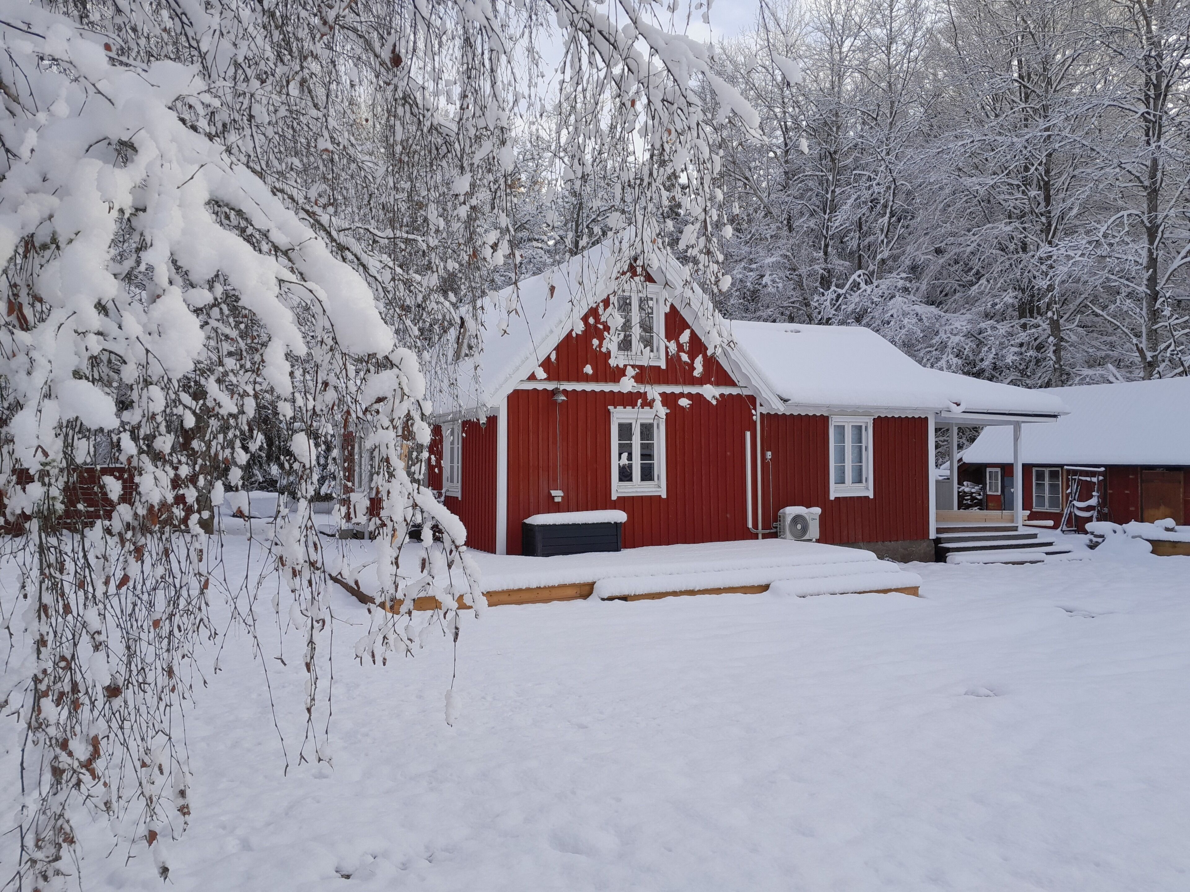 A red wooden house with a snow-covered roof and a porch.
