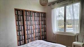 Una camera da letto con una grande libreria, un letto con copripiumino a pois, una sedia e una finestra vista alberi.