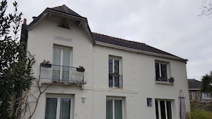 Un edificio su due piani con un balcone al piano superiore, una porta con un vetro e un piccolo giardino antistante.