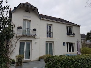 Ein zweigeschossiges Gebäude mit einem Balkon im oberen Stockwerk, einer Glastür und einem kleinen Garten davor.