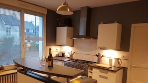 Una cucina moderna con isola centrale, piano cottura a gas e forno integrato. Sono presenti due sgabelli da bar e una finestra con persiane.