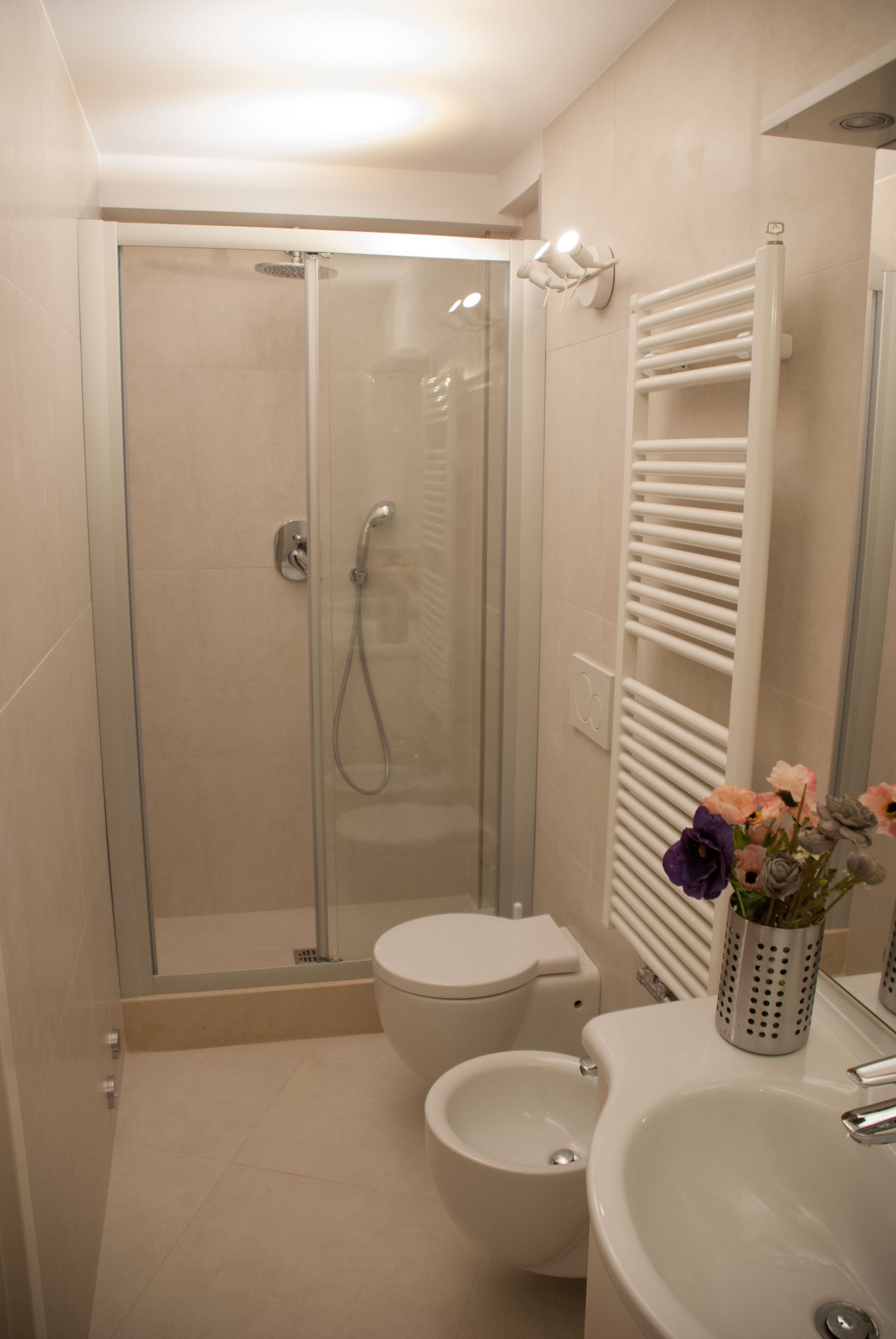 A modern bathroom with a glass-enclosed shower, a toilet, a bidet, and a sink with a decorative vase.