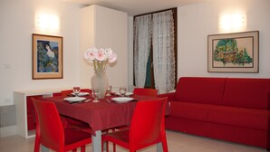 A dining area with a red table and matching chairs, a vase with flowers, and two framed artworks on the walls.