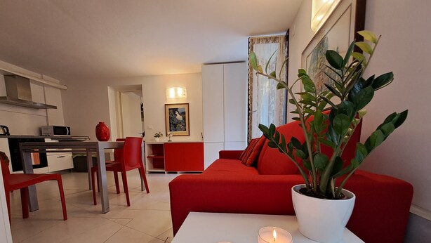 A modern living room with a red sofa, a white coffee table with two candles, and a potted plant.