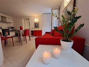 A modern living room with a red sofa, a white coffee table with two candles, and a potted plant.