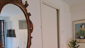 A room with a large ornate mirror, a white door, a small table with candles, a red chair, and a framed painting on the wall.