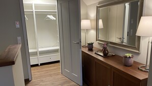 A walk-in closet with hanging space, a vanity with a mirror, and a wooden countertop with two lamps and a vase. - Exclusive maisonette vacation apartment (Coesfeld)