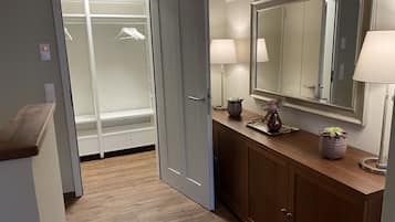 A walk-in closet with hanging space, a vanity with a mirror, and a wooden countertop with two lamps and a vase.